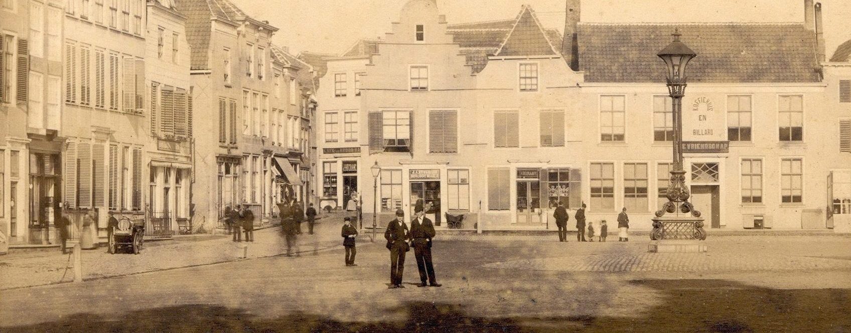De Grote Markt gezien in noordelijke richting met blik op de Opril, waar de reclame 'Koek en brood' te lezen is. Achter de lantaarn is te zien Koffiehuis en billiard De Vriendschap. Diverse mensen op straat.