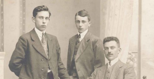 Portret van man met snor en stropdas, zittend, en twee jongemannen met stropdas, staand.