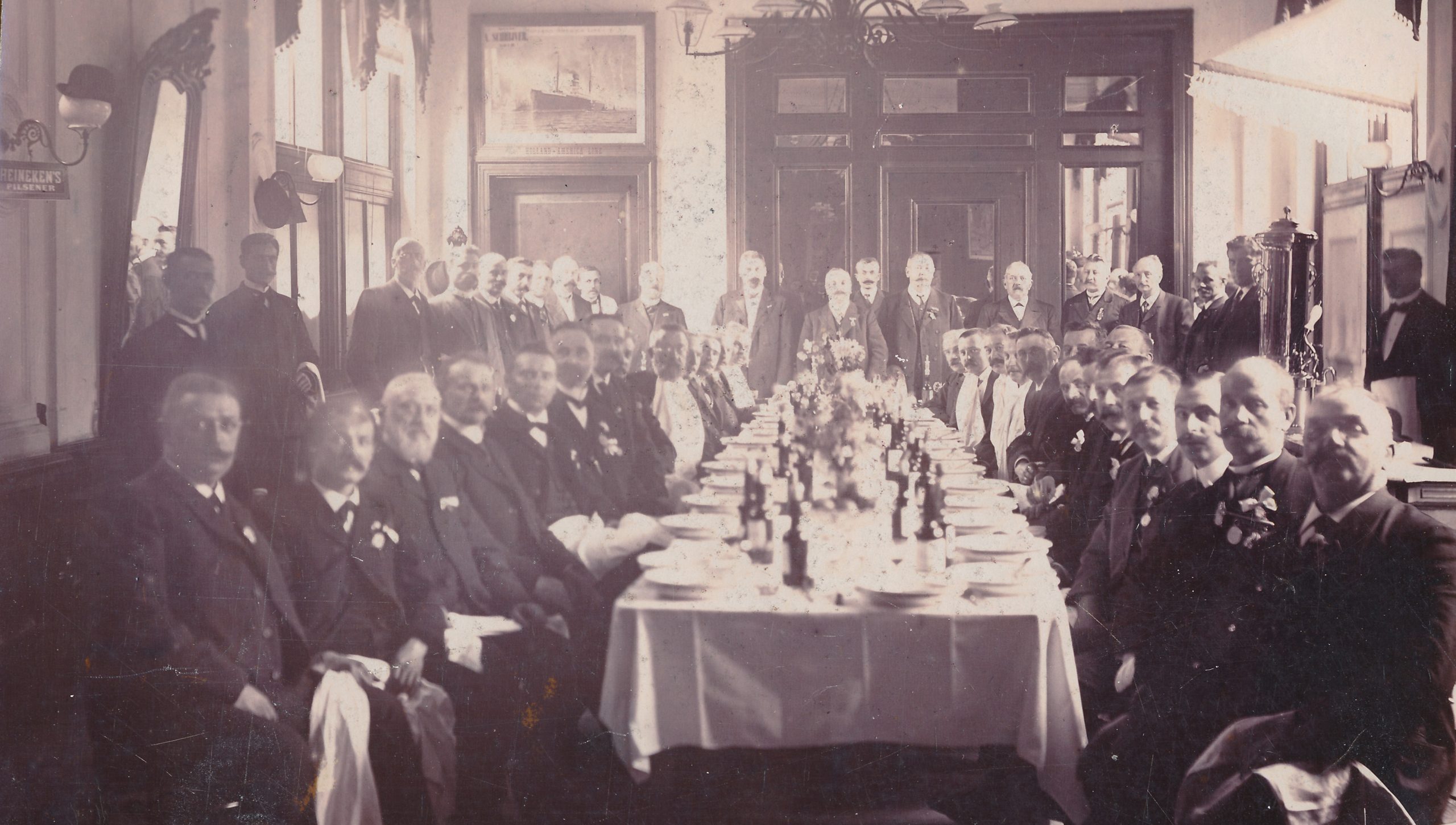 Foto van groot gezelschap heren aan tafel in horecagelegenheid.