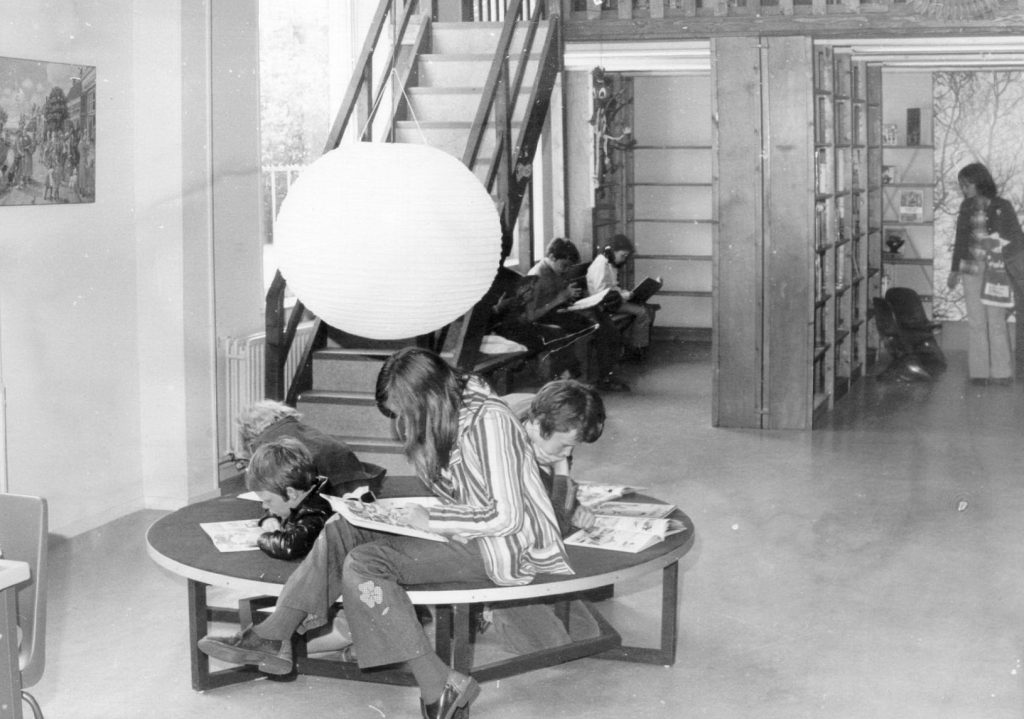 Boekenkasten en kinderen die zitten te lezen op de kinderafdeling van de bibliotheek